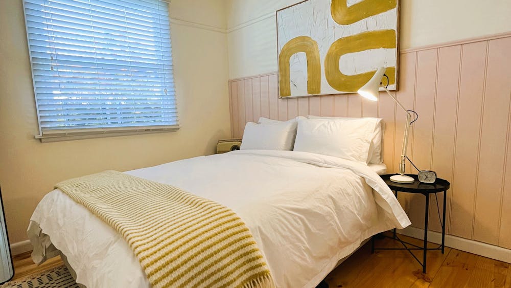 Queen bed, blanket and pink wainscoting, big painting and window.