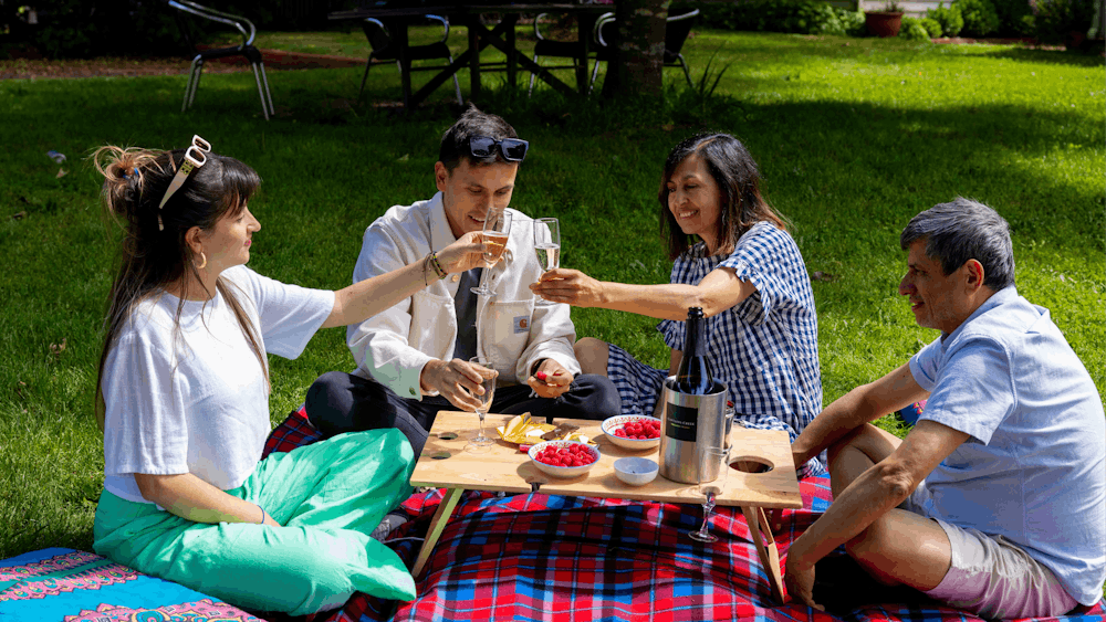4 people sitting on tartan picnic rug with large cushions.  Dessert and sparkling wine on the table