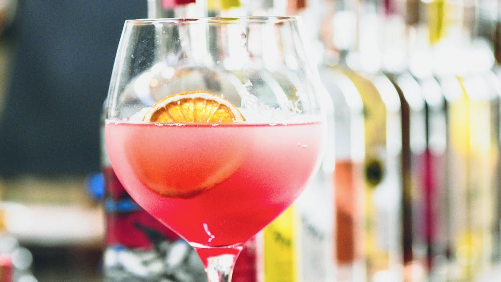 A cocktail on a bar in front of a row of gin bottles