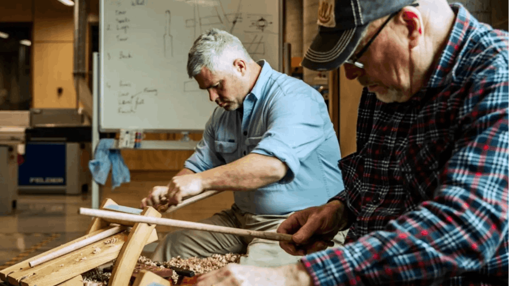 Two men seated and carving wood inside workshop