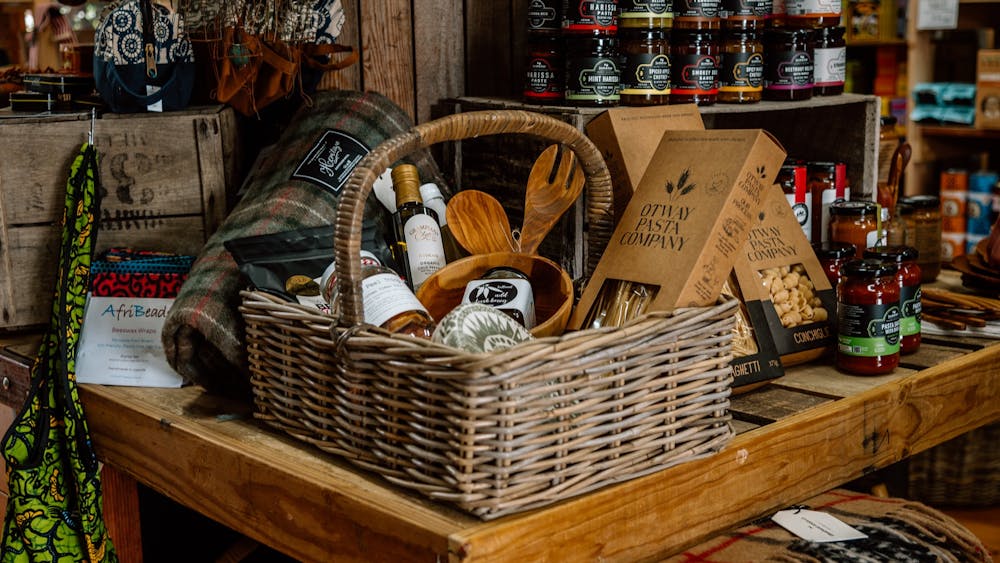 A wicker basket with a handle filled with pantry items and wooden utensils. next to wool blanket.