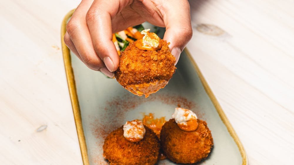 Hand holding one of three fried Arancini balls