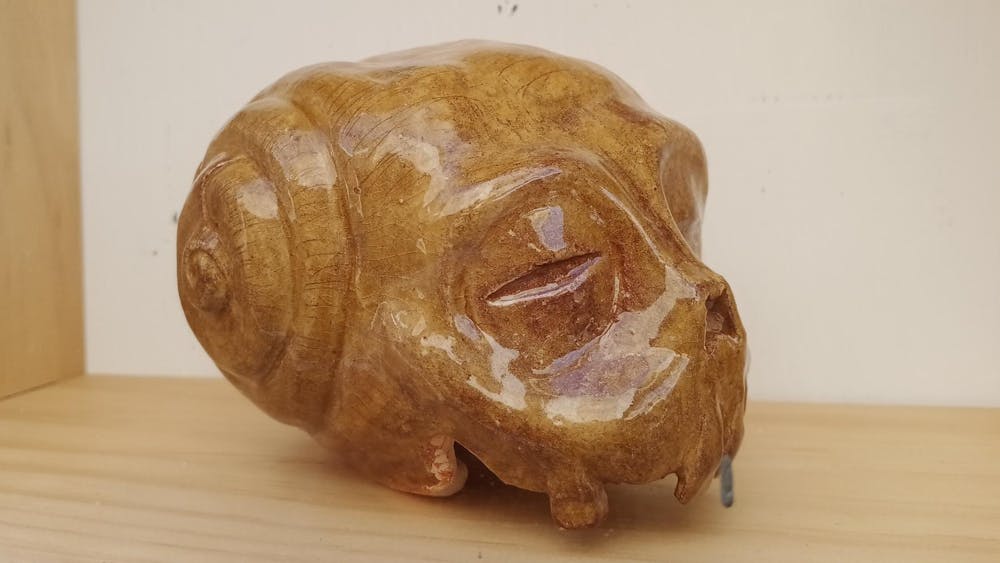 Ceramic sculpture of a morphing skull with a golden brown colour placed on a shelf.