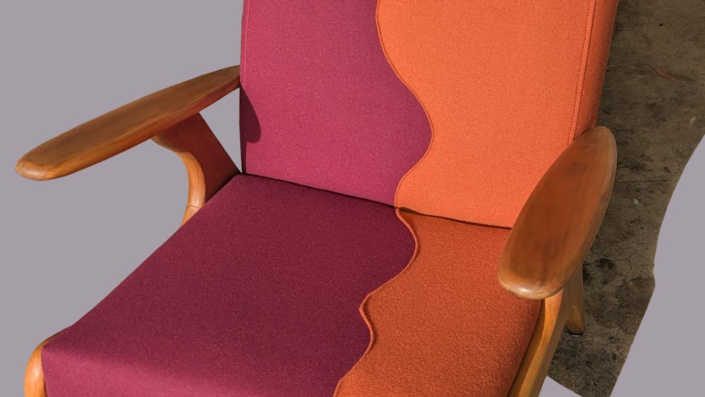 A wooden chair re-upholstered in bright orange and burgundy fabric.