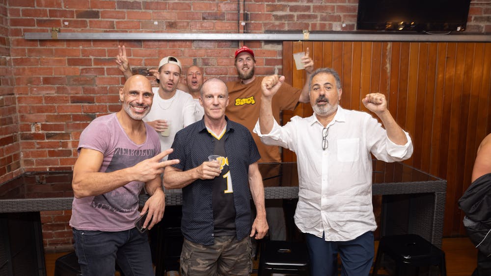Group of men holding drinks and posing for a photo inside Freight Bar during a Labour Day Eve party.