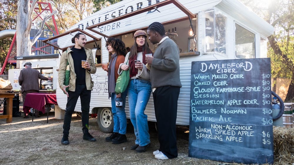 Two men and two women standing and drinking in front of Daylesford Cider van