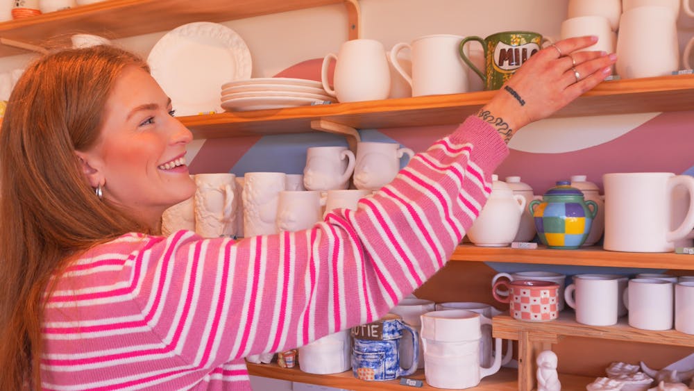 A women in a pink stripe top reaching for a pottery item on shelves