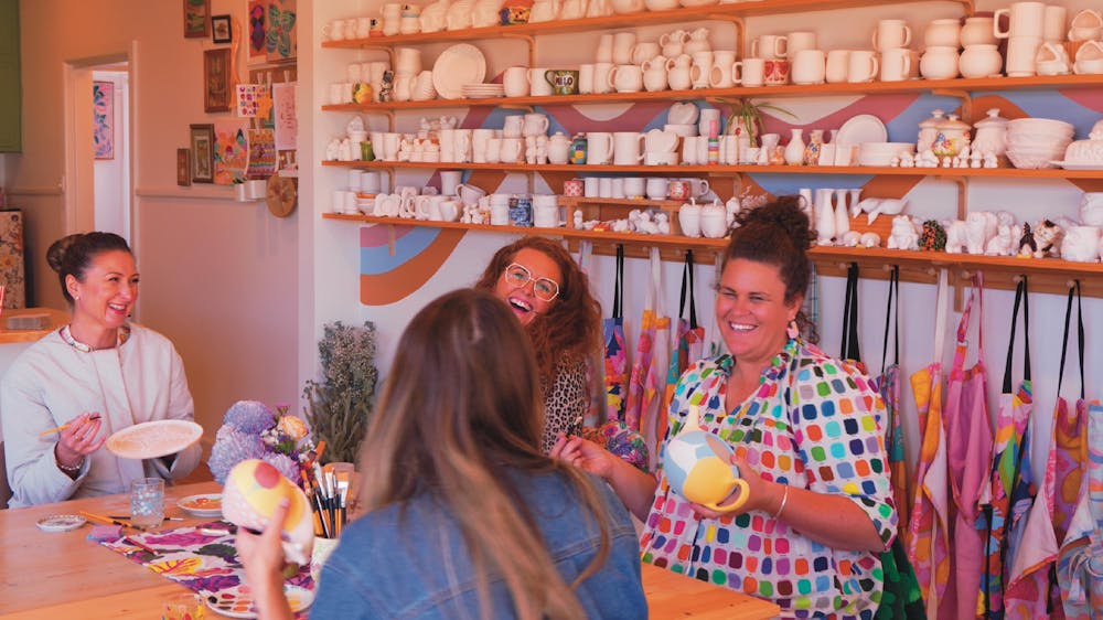 Four women laughing and smiling  whilst painting