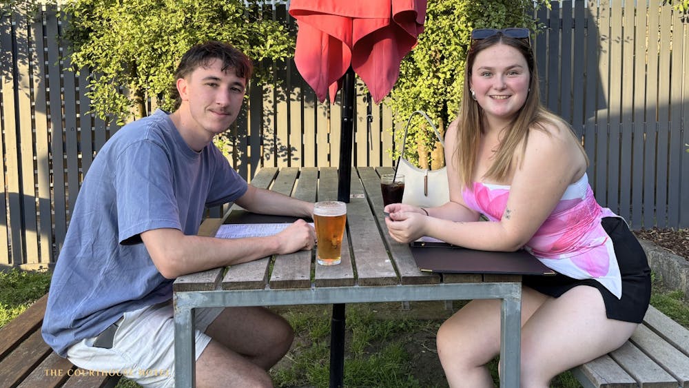wo guests sitting at an outdoor table with drinks, relaxing in the Courthouse Hotel beer garden.