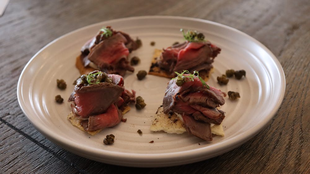 White plate containing four canapes of rare beef on top of crackers