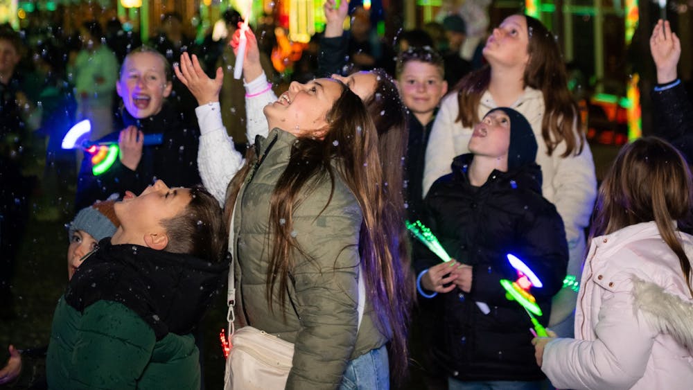 Children catching fake snow during Winter Wonderlights with lights in the background