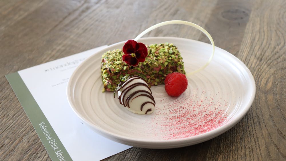 A rectangle of pistachio crusted parfait with berries on a white plate