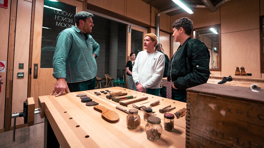 Man and woman speaking to maker beside a table full of tools