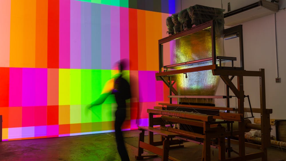 a person walks past the jaquard loom with a projection artwork on the wall