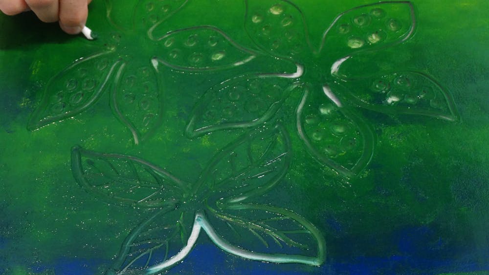 A hand makes marks into a painted surface