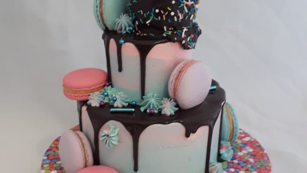 In tones of pink, blue and purple a two tier cake  with macarons and an ice cream cone on top