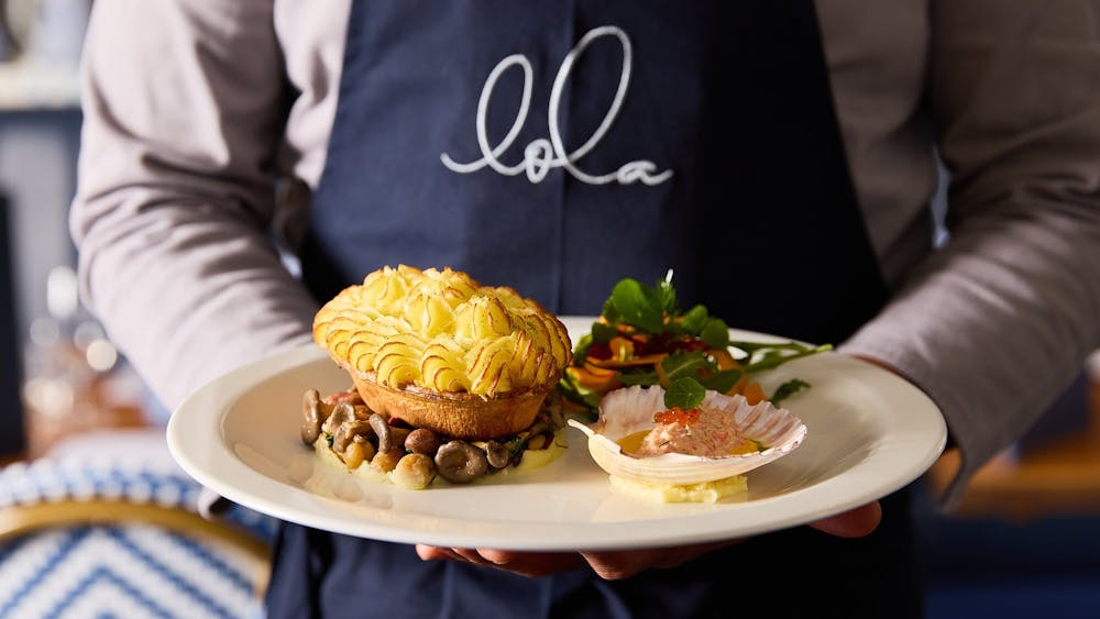 A chef holding a plate with a pie and side dishes