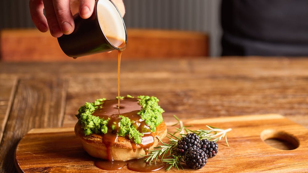 A pie on a wooden serving board with a glaze being added