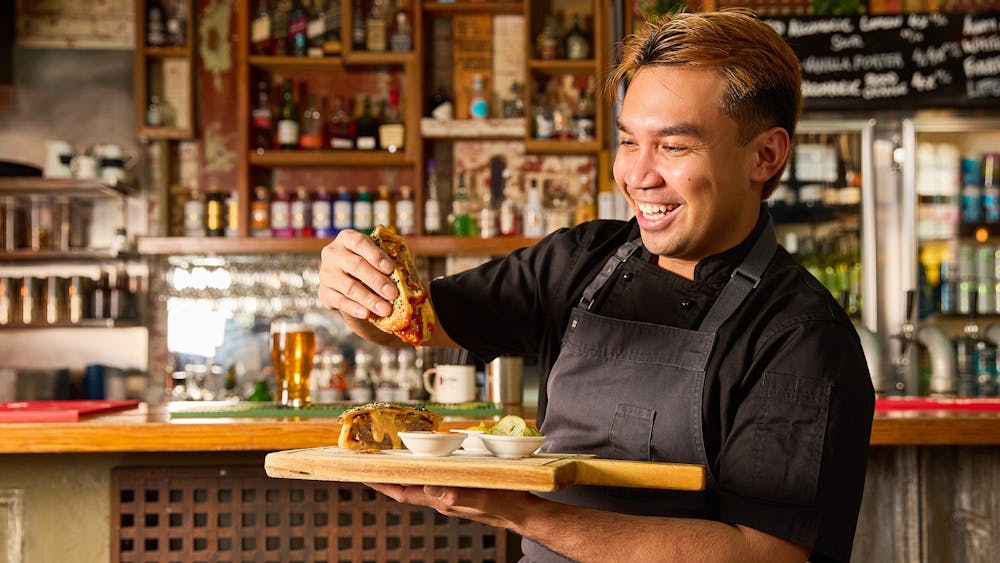 A chef holding an oozing cheeseburger pie and wooden serving tray