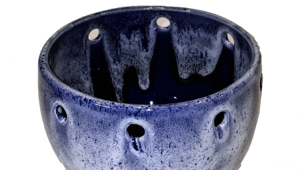 Ceramic bowl with holes around the rim with various shades of blue glaze.