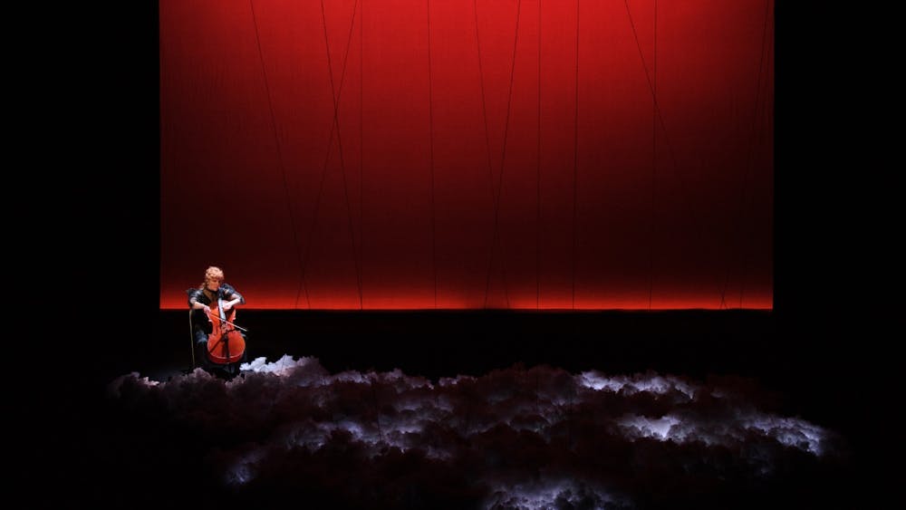 Zoë Barry playing cello on a red background with a cloud flashing with lightning beneath her