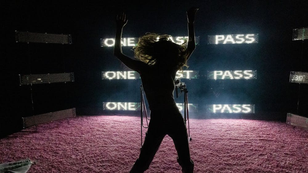 Girl dancing on a pink carpet, with lights in the background that say 'one last pass'