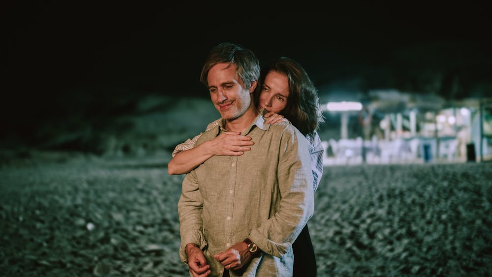 Two people standing on a beach, one hugging the other from behind