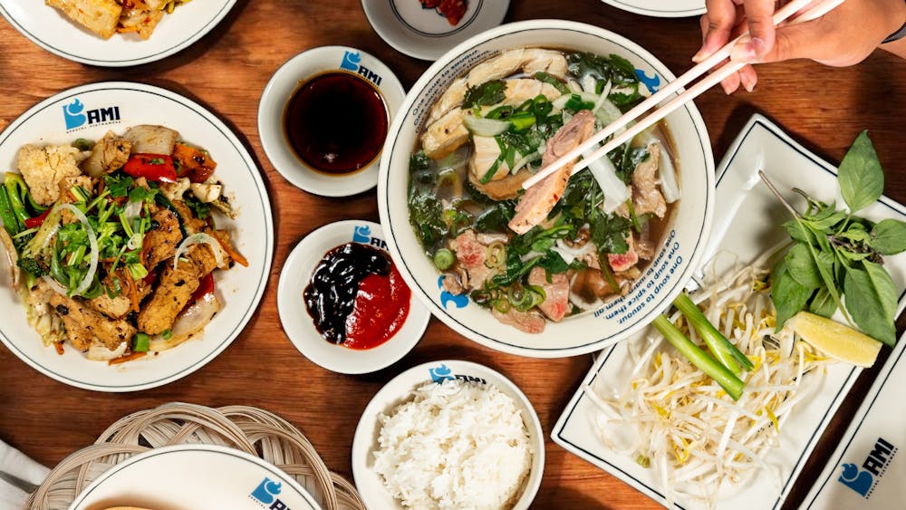 Overhead flatlay of Bami Vietnamese dishes on a timber table including pho broth with chopsticks