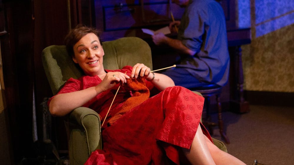 Nancy (Emily Goddard) in a bright red 1950s dress, knitting and smiling