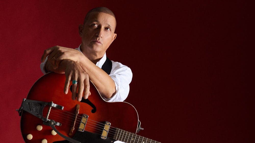 DIESEL dressed in white with an electric guitar on his lap against a dark red background