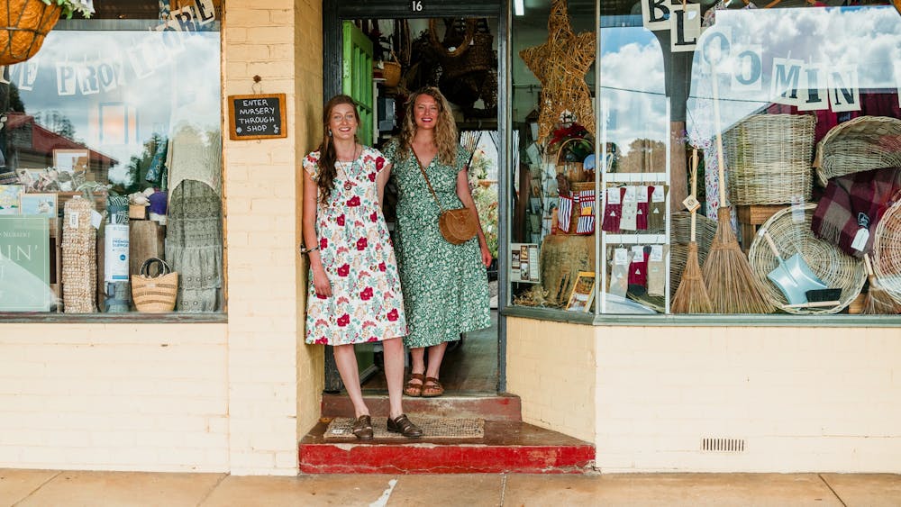 Two women in floral dresses stand outside a small boutique shop.