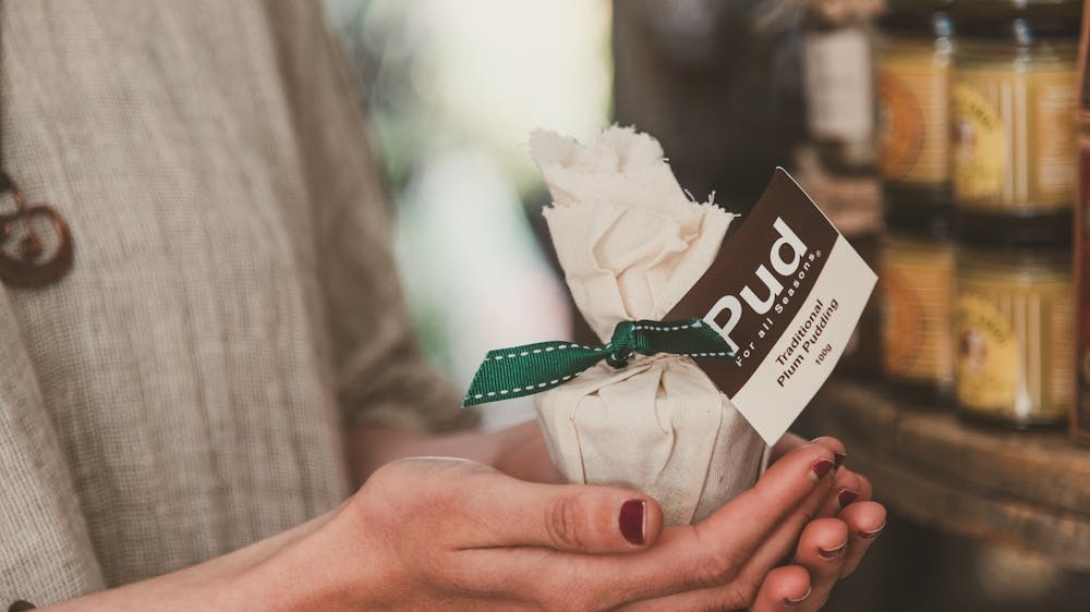 A pair of hands holds a small wrapped Christmas pudding.