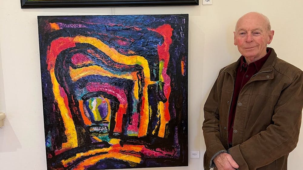 Russell is pictured with 2 of his dynamic, colorful abstract acrylic paintings.