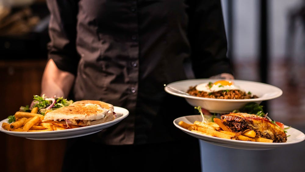 Staff member carrying three freshly prepared meals through the restaurant.