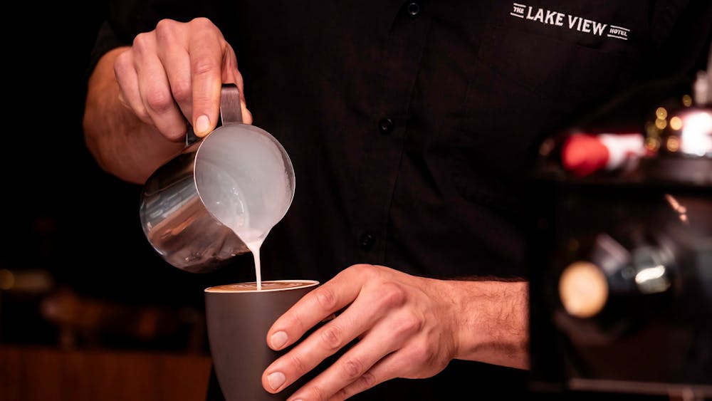 Barista pouring steamed milk into a freshly brewed coffee.