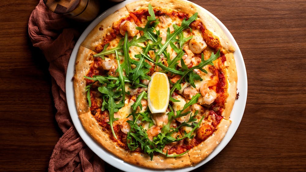Seafood pizza topped with prawns, salmon, rocket and lemon on a wooden table.