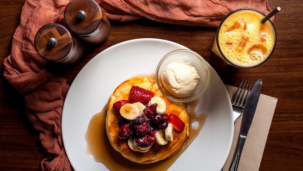 Stack of pancakes topped with fresh berries, banana, maple syrup and ice cream, served with juice,