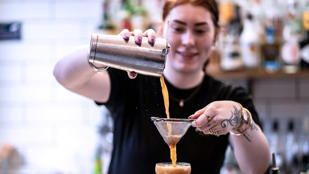 Bartender straining a freshly made cocktail into a coupe glass behind the bar at The North Star