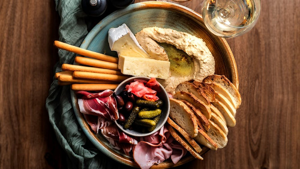 Share platter with cheeses, cured meats, hummus, pickles, bread and crackers, served with wine