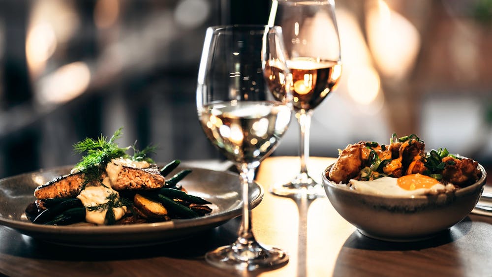 Dining table with a salmon dish, a chicken rice bowl and glasses of wine inside The North Star Hotel