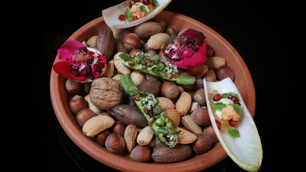A terracotta dish filled with assorted nuts and topped with colourful bite-sized degustation dishes