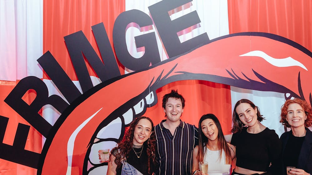 Six people smile and pose together at an event in front of a large red-and-white inflatable mouth an