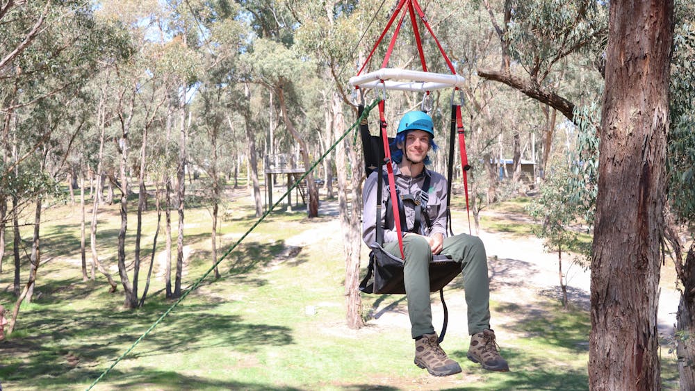 A camper uses an adaptive suspended harness on a zipline