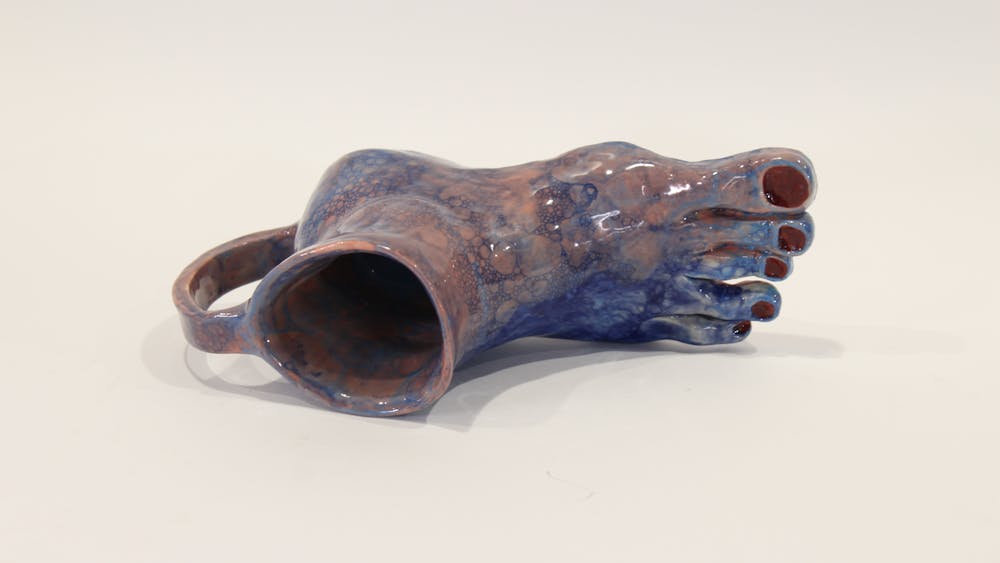 Pottery of a mug that features a human foot as the base of the mug.