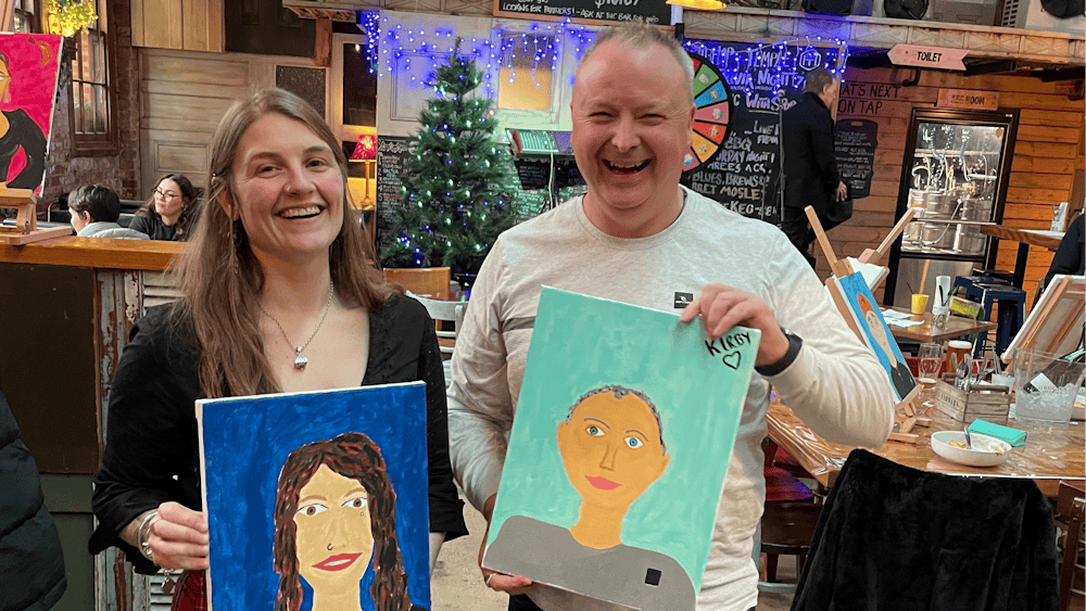 Two People hold painted portraits of each other in Hop Temple