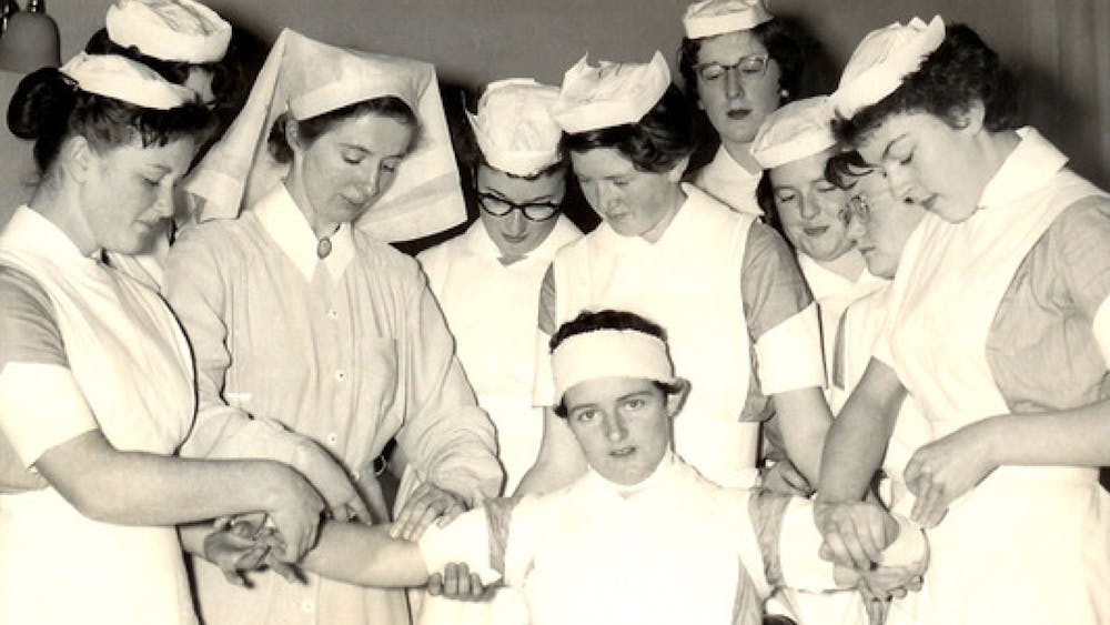Black and white photo of nurses practicing bandages on one another - July 1958