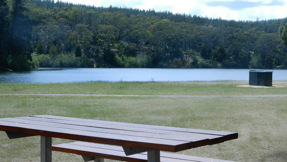 Standing behind a picnic table looking out and over the the nearby St Georges Lake with blue skies