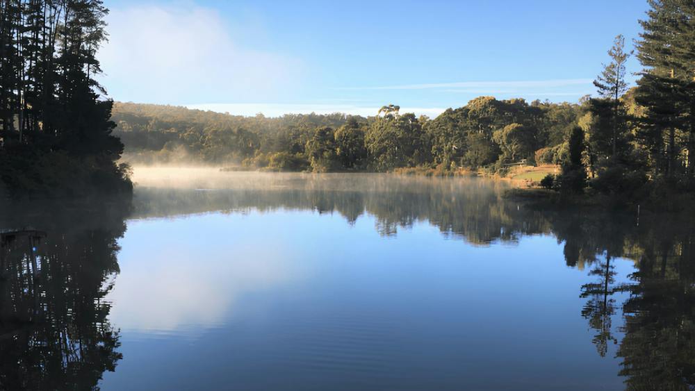 Standing on the bank of St Georges Lake looking out to the reflective water with blue skies & trees