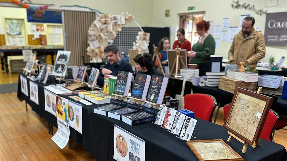 Foreground features tables covered in black cloth featuring books. People browse in the backgroun.d