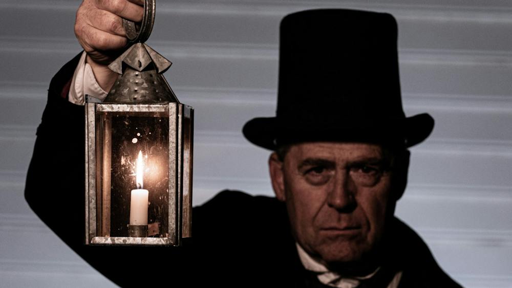 Man dressed in black jacket, white shirt and top hat holding up a lantern